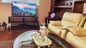A living room with a television, a sofa, a coffee table with teapots, and a decorative clock on the wall. - Chinese style suite near golf course (Surrey)