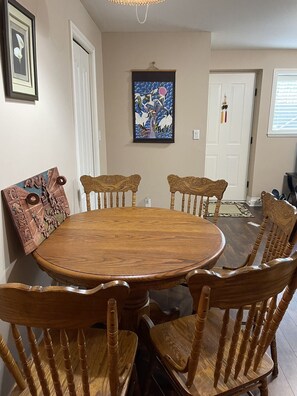 A dining room with a round wooden table surrounded by six wooden chairs with carved backs. There are framed artworks on the walls, a door with a decorative handle, and a window with blinds. - Chinese style suite near golf course (Surrey)