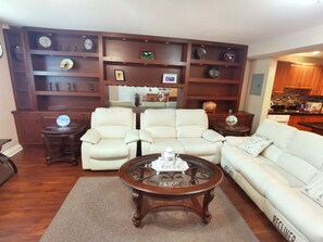 A living room with a sofa, two armchairs, a coffee table, and a wooden bookshelf with clocks and decorative items. - Chinese style suite near golf course (Surrey)