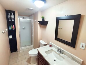 A bathroom with a toilet, sink, and shower. There is a shelf with toiletries and a mirror on the wall. - Chinese style suite near golf course (Surrey)