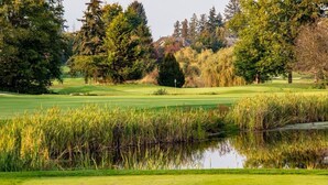 A golf course with a pond in the foreground, surrounded by trees and a clear sky. - Chinese style suite near golf course (Surrey)