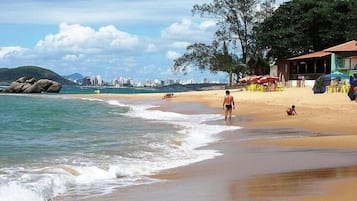 Una playa con una persona caminando, un niño jugando y un edificio con terraza.