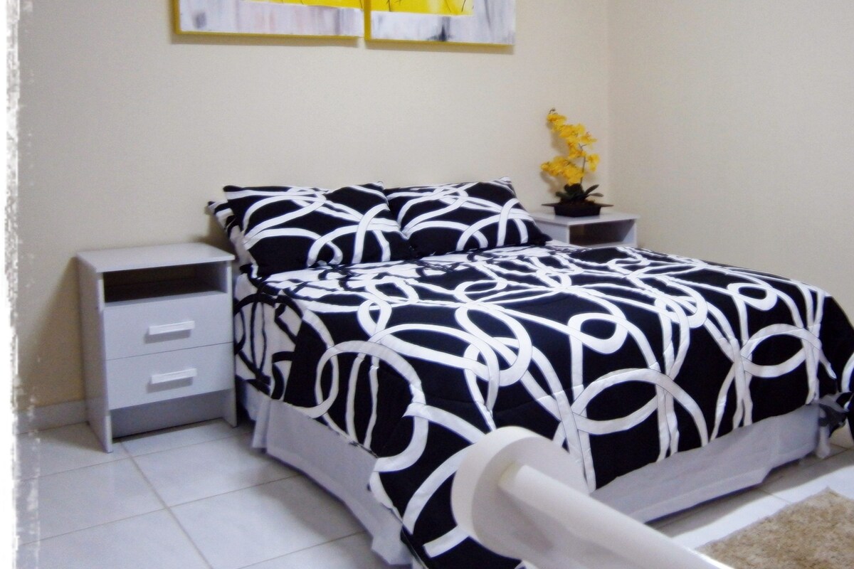 A bedroom with a bed, bedside tables, a nightstand, a potted plant, and a door.