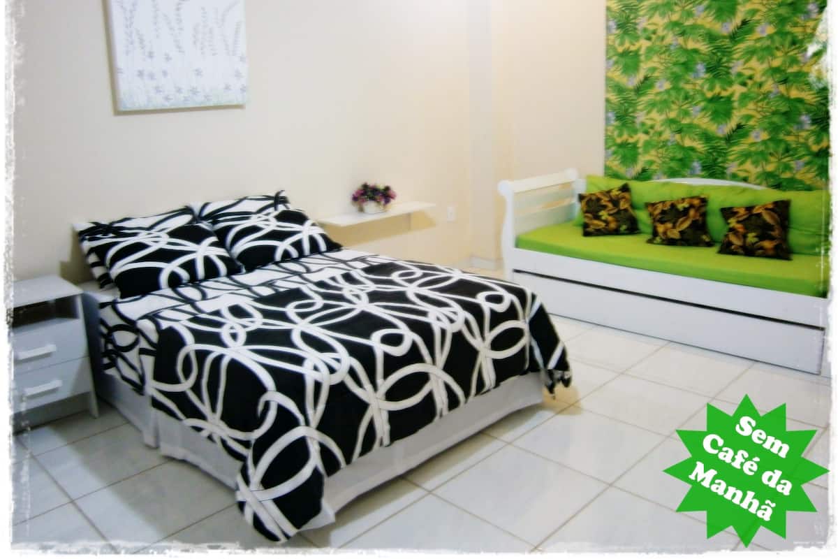A bedroom with a bed, a nightstand, a dresser, a green sofa with cushions, and a wall with a leafy pattern.