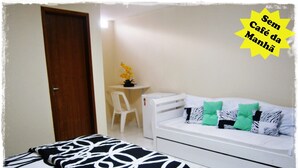 A bedroom with a bed, a white sofa, and a small table with a plant. - Hospedaria Oca Ruca (Guarapari)