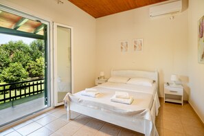 A bedroom with a bed, two bedside tables, a nightstand, a window with a view of greenery, and a ceiling fan.