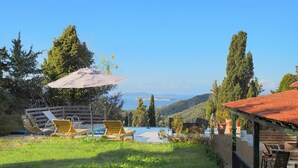 A pool area with lounge chairs and an umbrella, surrounded by greenery and hills in the background. - Escape to Serenita Villa in Arillas, Corfu - Private Pool, Sunset Views, and More (Arillas)