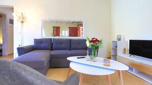 A living room with a sectional sofa, a white coffee table, a flat-screen TV, and a mirror reflecting the room.