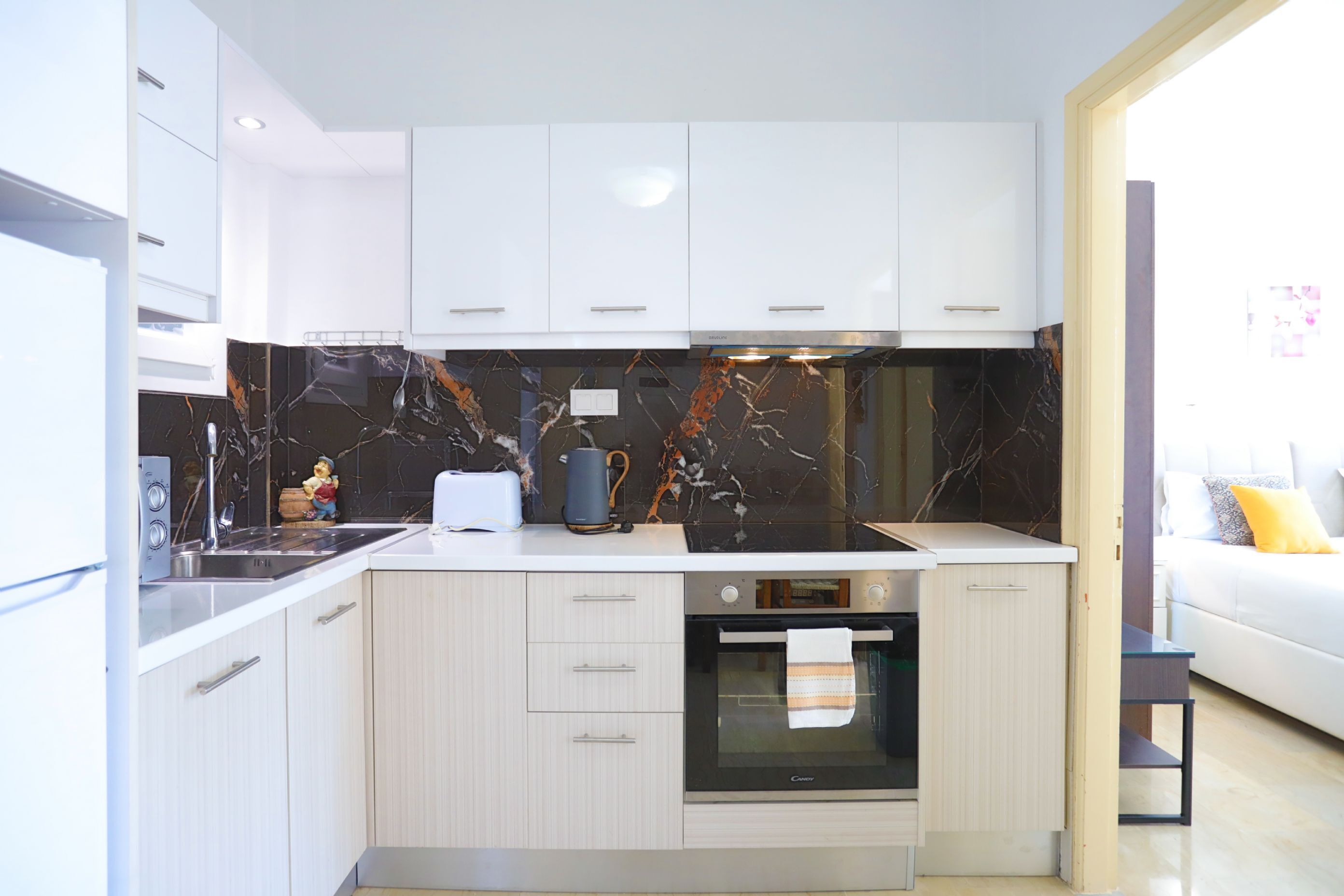 Una cocina moderna con armarios blancos, salpicadero de mármol y horno empotrado.