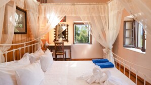 Een slaapkamer met een hemelbed, een bureau met spiegel en een raam met uitzicht op groen.