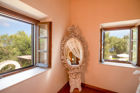 Una habitación con dos ventanas, un espejo grande y decorado, y vista a zonas verdes al exterior.