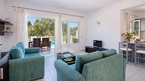 A modern living room with teal sofas, a flat-screen TV, and a dining area with a table and chairs. - Stylish Hideaway, 2-mins from Marmari Beach! (Loggos)