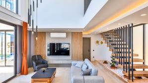 Un salon moderne avec un canapé, une table basse et un téléviseur. On y trouve un escalier avec des marches en bois et une rampe.