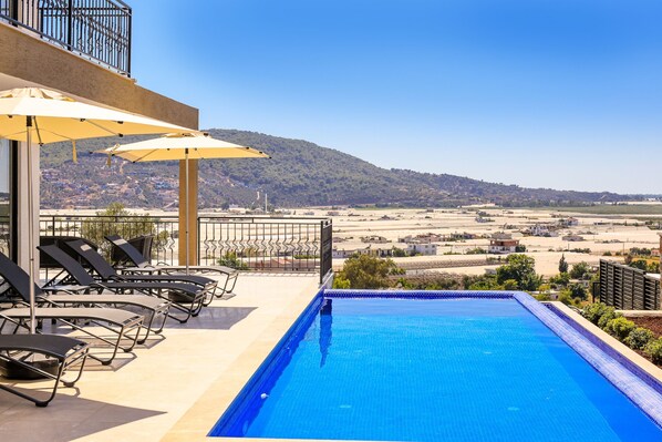 Piscina com vista para uma paisagem distante, espreguiçadeiras e guarda-sóis.