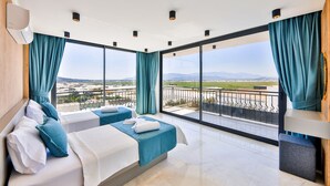 Une chambre d’hôtel avec deux lits, de grandes fenêtres et un balcon offrant une vue sur la ville et les montagnes.