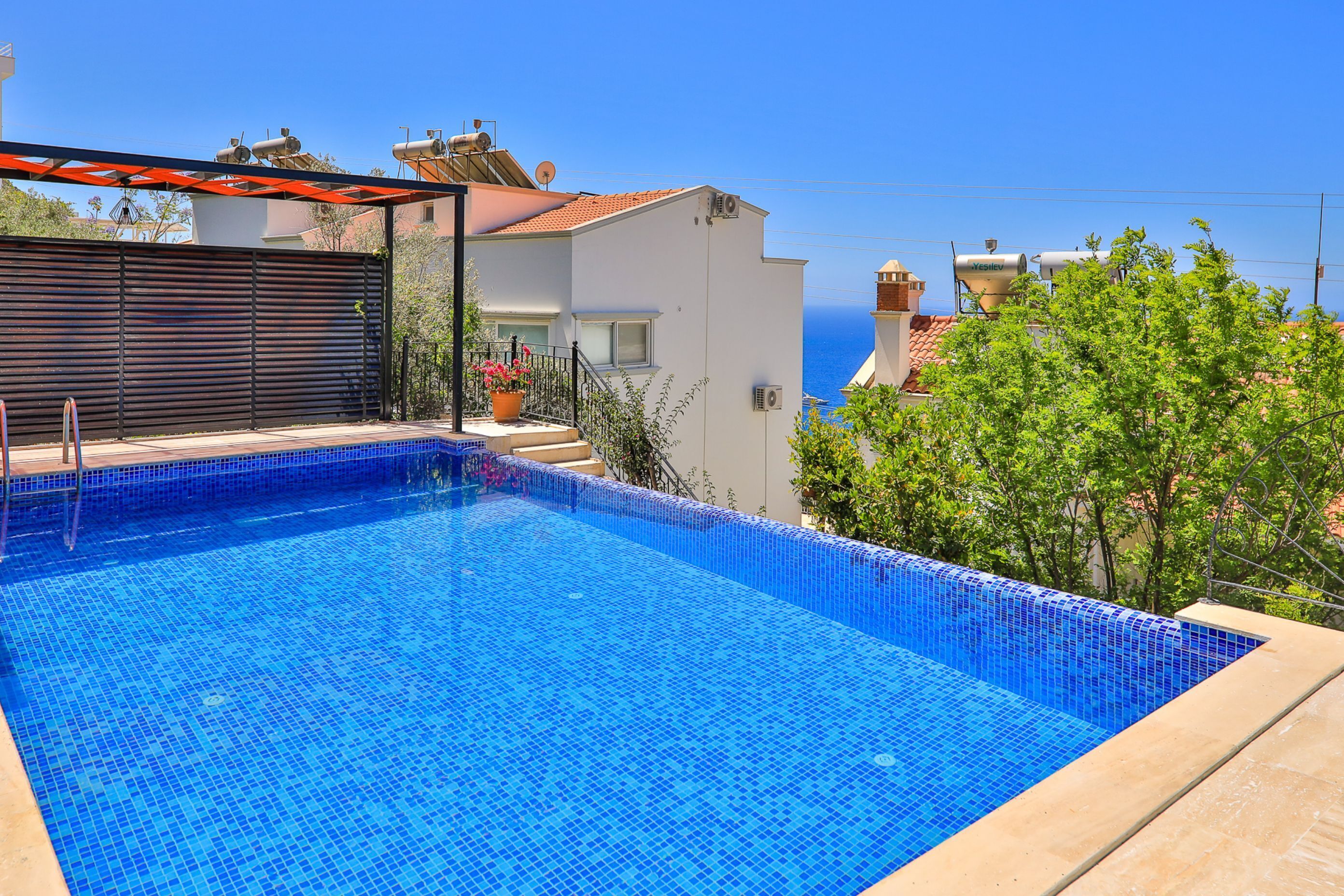 A swimming pool with blue mosaic tiles, surrounded by a beige deck.