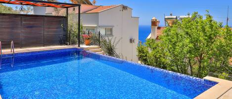 A swimming pool with blue mosaic tiles, surrounded by a beige deck.