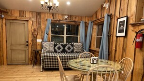 A cozy room with a wooden interior, a checkered sofa, a glass table, and wooden chairs. - Pacific Coast Highway Milkhouse (San Luis Obispo)