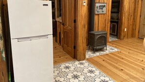 A kitchen with a white refrigerator, wooden walls, a tiled floor, and a small wood-burning stove. - Pacific Coast Highway Milkhouse (San Luis Obispo)