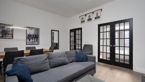 Ein modernes Wohnzimmer mit einem grauen Sofa, einem Esstisch mit Stühlen und schwarzen Türen mit Glasverzierungen.