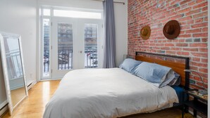 Ein Schlafzimmer mit einem großen Bett, einer Ziegelwand und Blick durch eine Glastür.