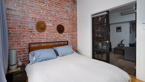 Ein Schlafzimmer mit Backsteinwand, einem Bett mit weißer Bettwäsche und einer Tür zu einem Wohnbereich.