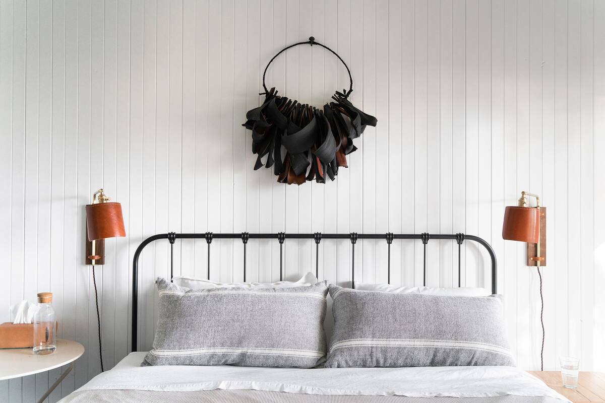 A bedroom with a metal bed frame, grey pillows, a white wall, and two wall-mounted lamps.
