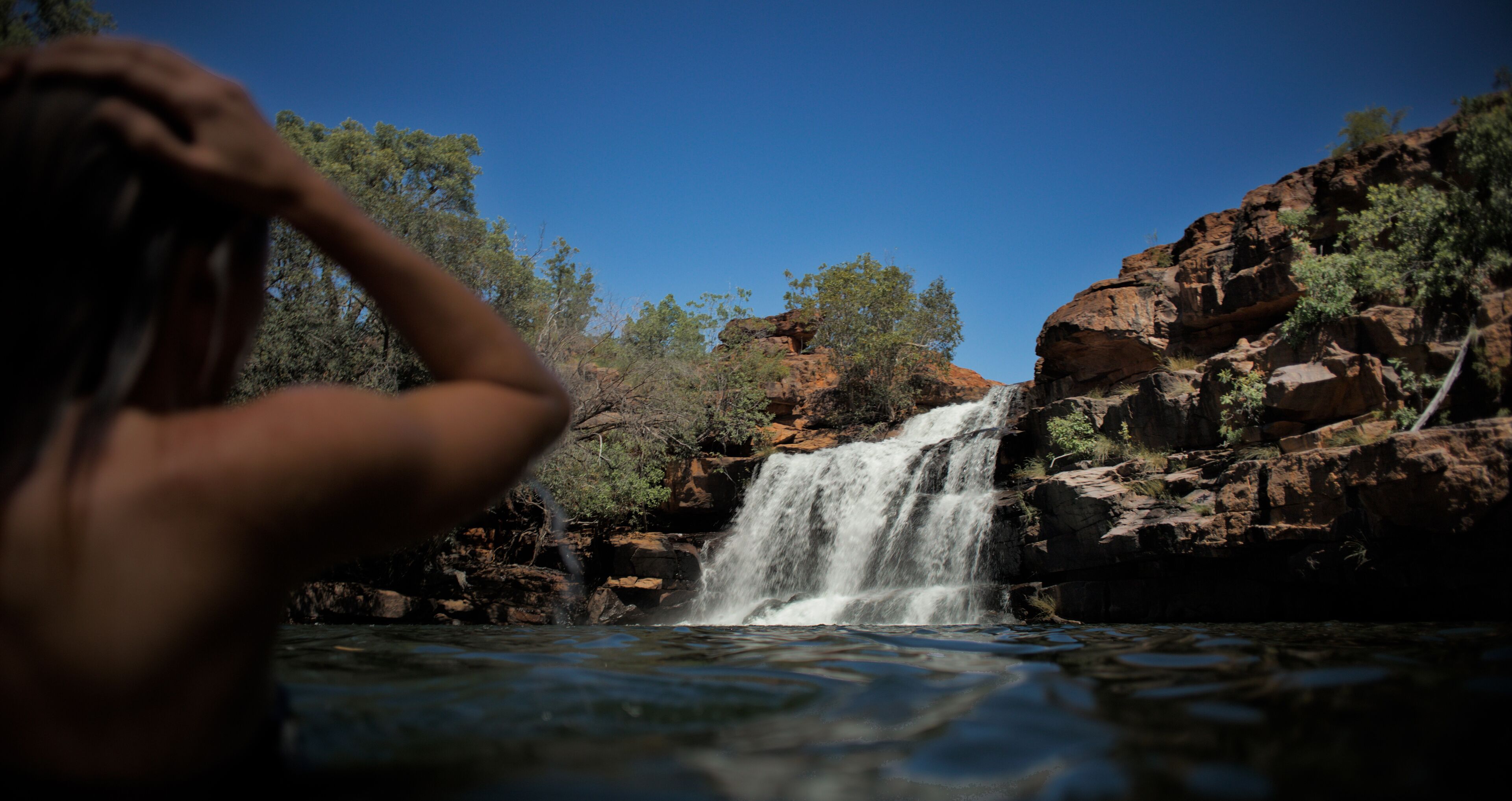 A waterfall in a natural setting with rocky terrain and sparse vegetation.