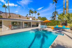 Ein modernes Haus mit Swimmingpool, Sitzgelegenheiten im Freien und Palmen.
