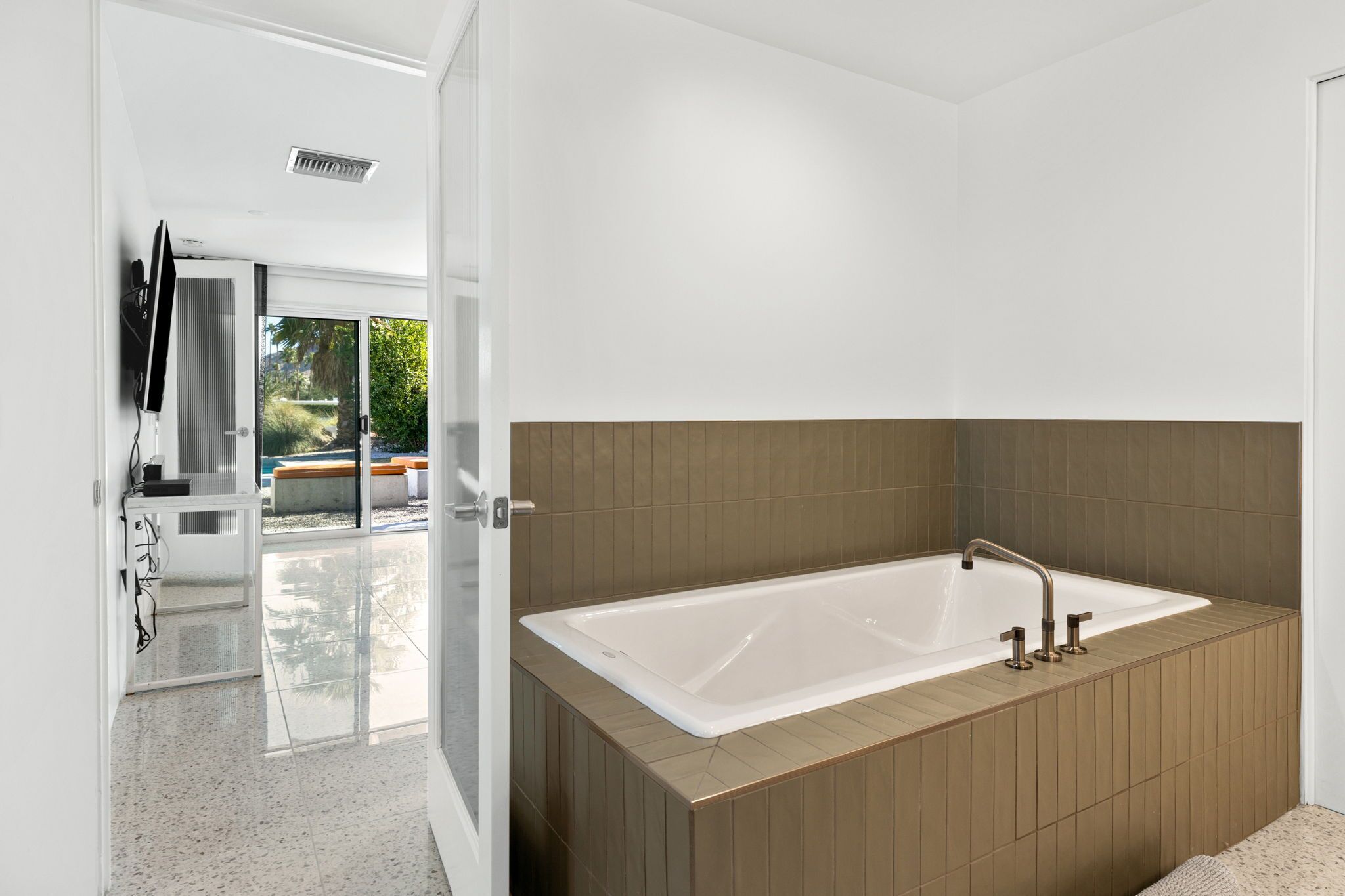 A modern bathroom with a large bathtub, a shower area, and a glass-enclosed door leading to an outdoor space.