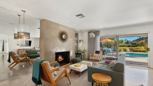 Een moderne woonkamer met een open haard, comfortabele zitplaatsen en uitzicht op een zwembad.