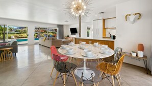Een moderne eethoek met een ronde tafel voor zes personen, omringd door transparante stoelen. Daarboven hangt een grote, bijzondere kroonluchter.