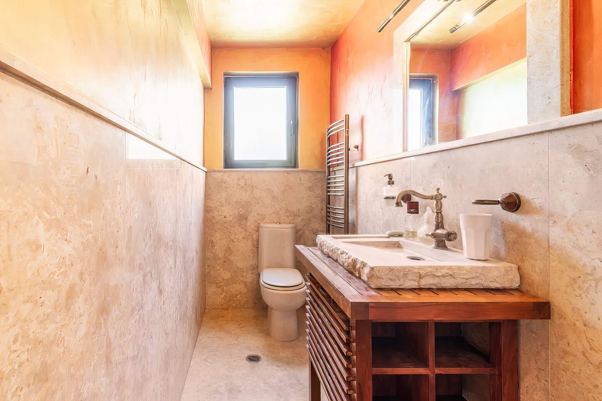 A bathroom with a marble sink, a toilet, a towel rack, and a window.