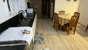 A kitchen with a black countertop and a patterned rug. There is a dining area with a wooden table and chairs. - Casa de Praia e Campo com Piscina (Garopaba)