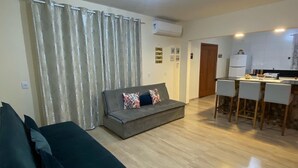 A living room with a sofa, a dining area with a table and chairs, and a kitchen with a refrigerator. - Casa de Praia e Campo com Piscina (Garopaba)