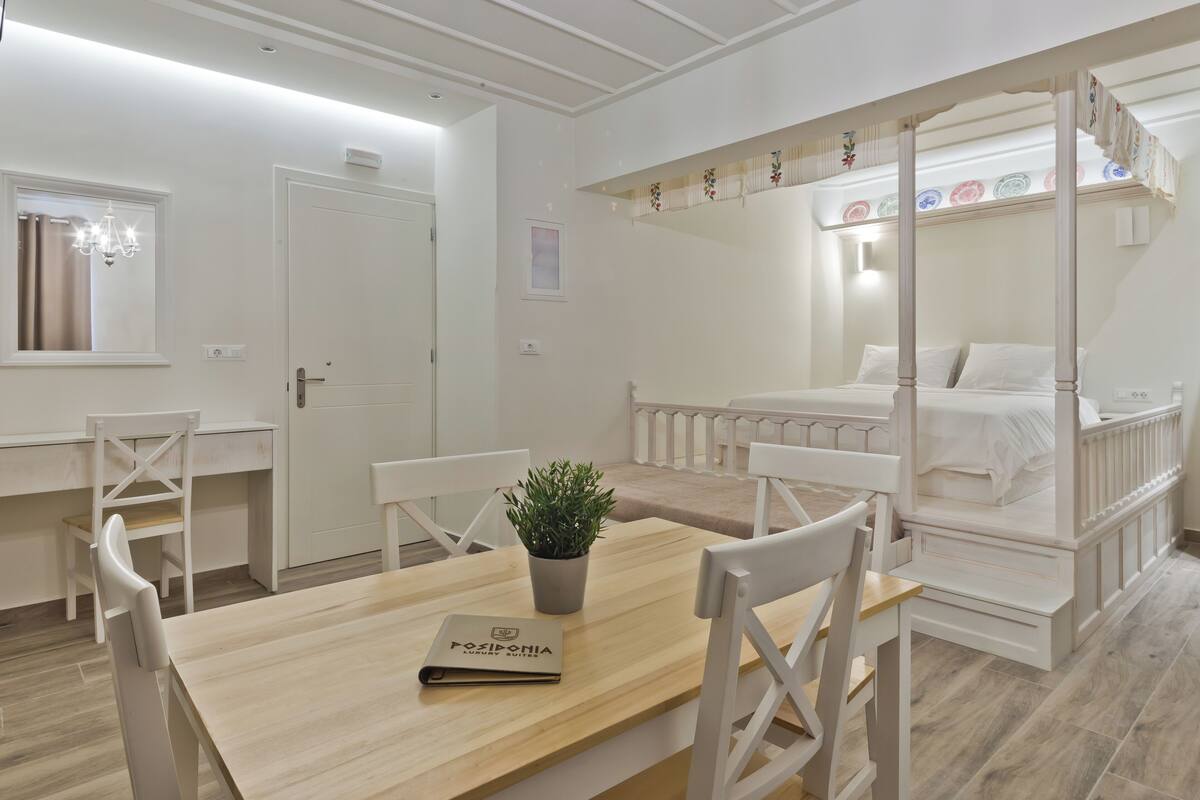 A bedroom with a four-poster bed, a wooden table with a plant, and a desk with chairs.