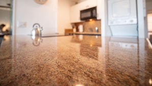 A kitchen with a granite countertop, a microwave, and a clock on the wall. - Great Location! Walk to Everything in South Kihei! (Kihei)