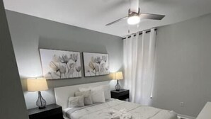 A bedroom with a bed, two bedside tables, a ceiling fan, and artwork on the wall. - Luxury 5bd home close to Disney parks private gated property  (Kissimmee)