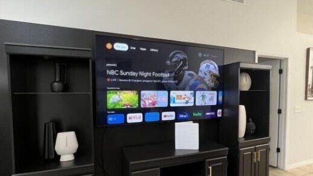 A modern living room with a large flat-screen TV mounted on a black entertainment unit. - Luxury 5bd home close to Disney parks private gated property  (Kissimmee)