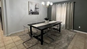 A dining area with a rectangular table, clear chairs, a chandelier, a painting on the wall, and a window with curtains. - Luxury 5bd home close to Disney parks private gated property  (Kissimmee)