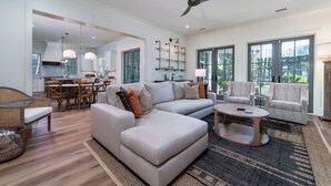 A spacious living area with a large sectional sofa, a round coffee table, and a dining area with a wooden table and chairs.