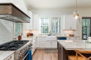 Une cuisine moderne avec des meubles blancs, une cuisinière en acier inoxydable et un grand îlot central doté d’un comptoir en marbre.