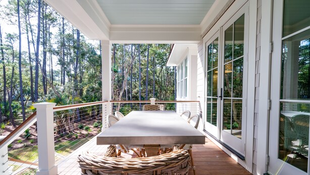 A covered outdoor area with a dining table and chairs, surrounded by glass doors and windows, overlooking a forested area.
