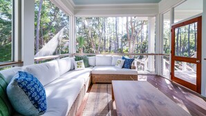 A covered outdoor seating area with a white wicker sofa, blue and green patterned pillows, and a wooden table.