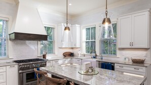 A modern kitchen with white cabinets, a large island, stainless steel appliances, and pendant lighting.