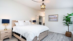 Een slaapkamer met een houten bed, nachtkastjes, een hanglamp, een ingelijst schilderij aan de muur en een potplant.