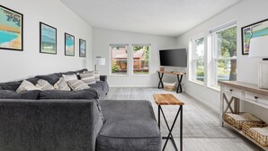 Een moderne woonkamer met een grijze bank, een houten salontafel en een televisie op een dressoir.