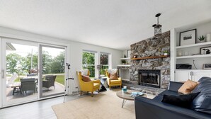 Een moderne woonkamer met een stenen openhaard, gele stoelen, een donkere bank en een glazen deur naar een terras.