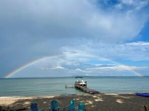 Una playa con un barco amarrado en el muelle, un arcoíris en el cielo y sillas turquesas sobre la arena.