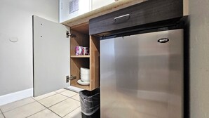 Eine kleine Küche mit Einbaukühlschrank, einer Holzhilfe für Küchenutensilien und einem Mülleimer.